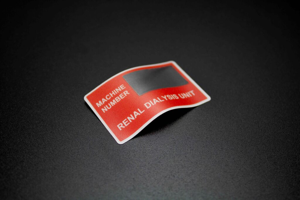 Red plastic asset label with white text and border and clear window for equipment labelling