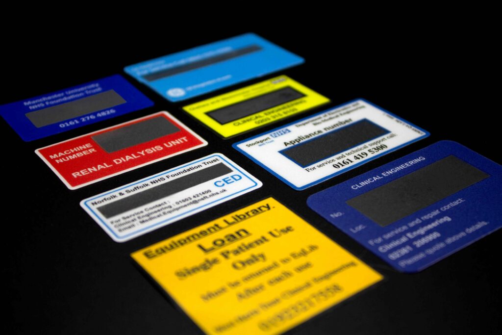 A range of colourful plastic asset labels with clear windows stuck flat to a surface