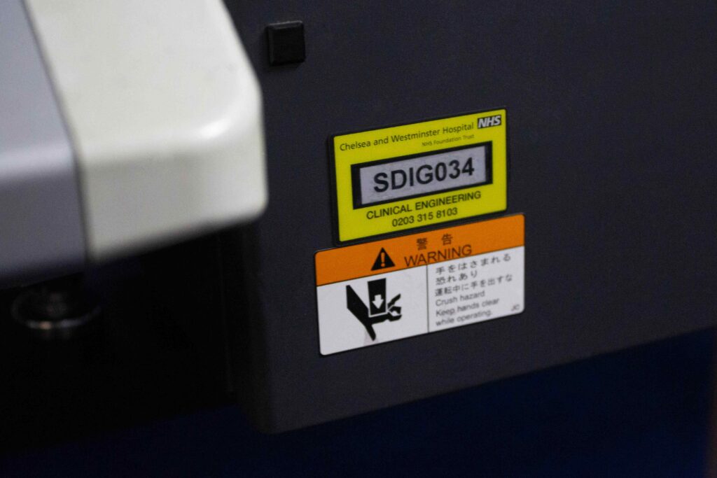 Black and yellow plastic medical label with serial numbering showing through clear window stuck to machine